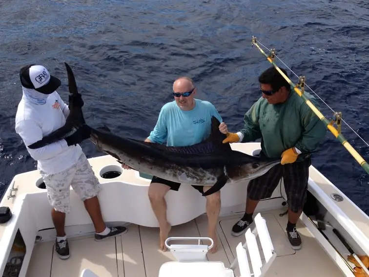 3 men on a boat holding a large marlin off the coast of Cabo San Lucas