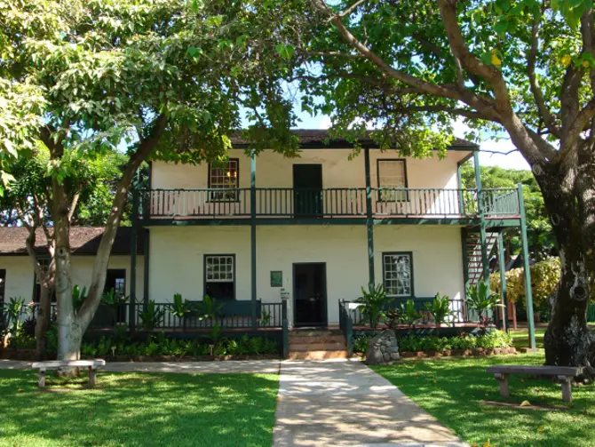 Front of Baldwin hom - white two story building each with symmetrical center doors and windows on either side. A porch runs along the length of the second floor. The home has a wide sidewalk leading to the front door and is shaded by large trees.