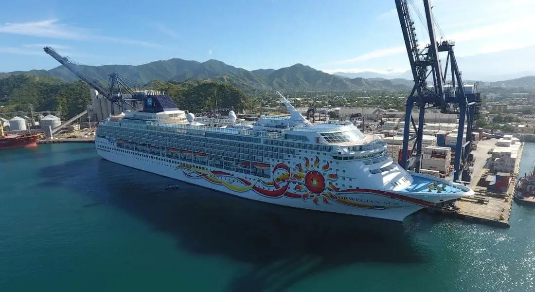 Cruise ship docked in Santa Marta next to cargo containers stacked on shore and a large crane