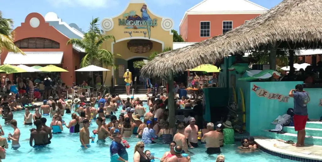 Inside of Margaritaville with people wading in large pool, thatched roof pool bar, surrounded by colorful buildings