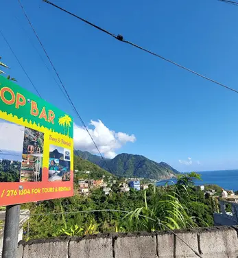 View of Roseau from hilltop with mountain in background and sign in the foreground left for