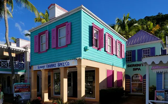 Sunny Caribee Spice company exterior - colorful square building with light orange painted bottom half,  around the entrance, upper is sided turquoise with large windows with bright pink shutters