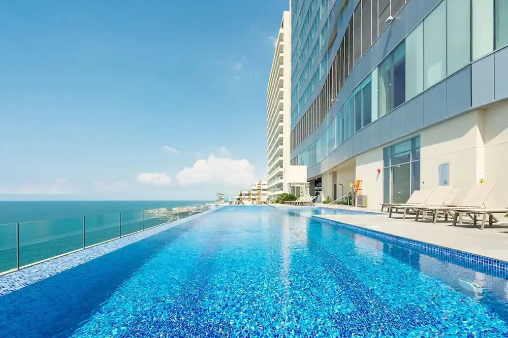 Side view of large white hotel building with a narrow infinity pool lined with lounge chairs