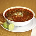 Bowl of pozole with bread and lime on the side
