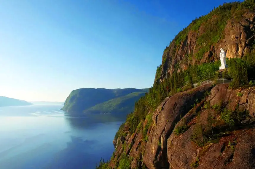Side view of white Madonna statue high up on the side of the cliffs which line with Saguenay fjord. 