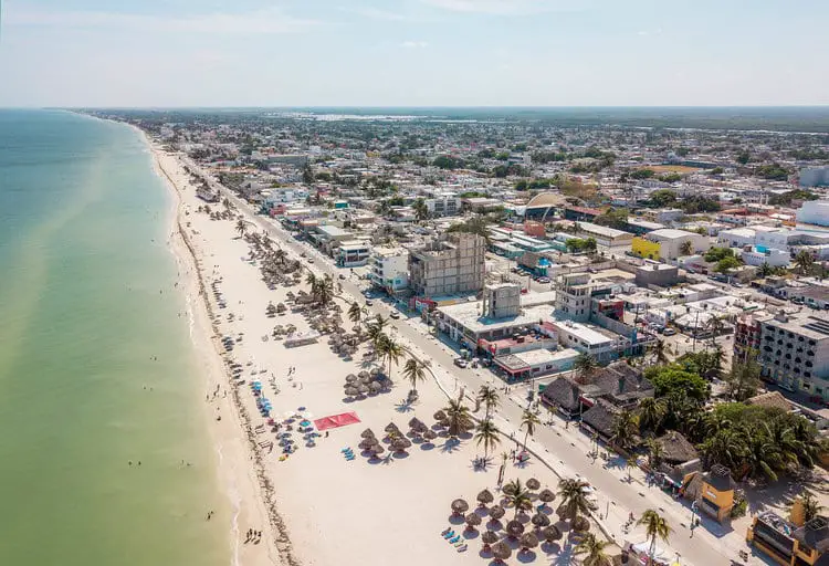 Aerial view of the beach and town. The beach is lined with small thatched-roofed huts. The town is crowded with buildings.