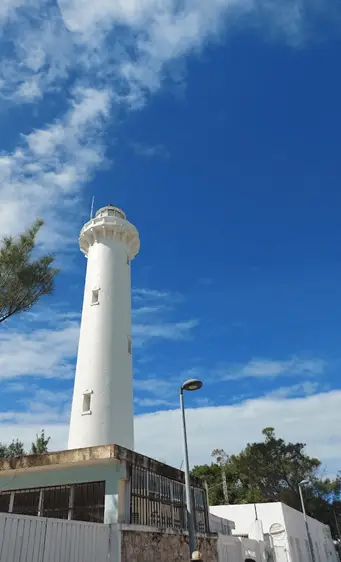 Looking from the ground up at a tall, white lighthouse against a blue sky with wispy white clouds.