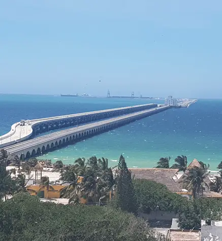 Looking from shore at the 4 mile long Progreso pier as it curves to the left and fades into the distance. You can see cargo cranes in the far distance at the end of the pier. 