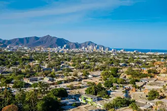 Aerial view of Santa Marta with mountains in the background. There are a small buildings with sand-coloured ground in between and sparse trees and greenery