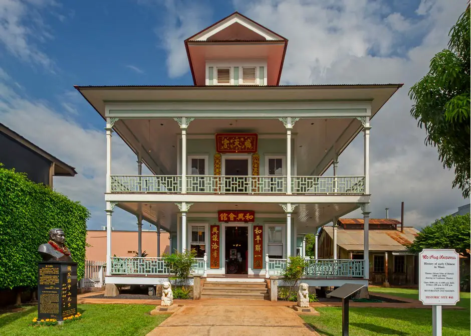 Two story building with large wrap-around porches and small peaked roof.