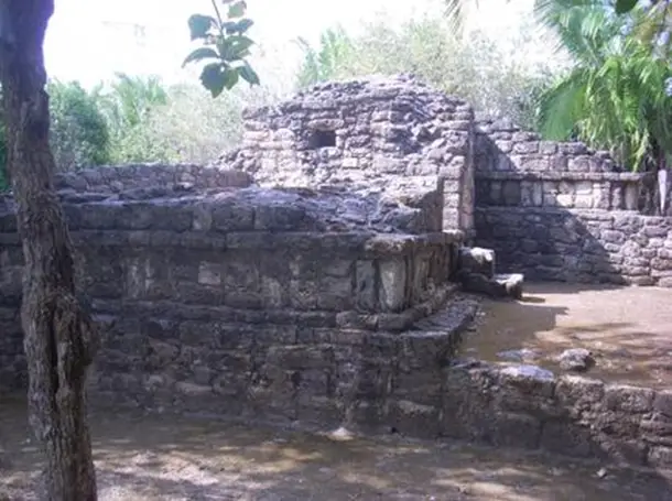 Stone ruins of a two-level building. Short walls are open and two stone steps lead up from the ground level to what was once a room