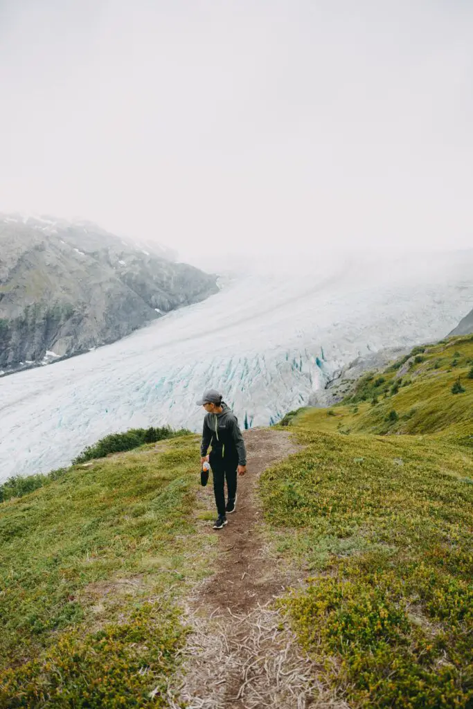Person hiking on a trail. A large white glacier and rocky outcropping is in the background.