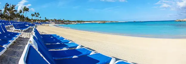 wide angle view of rows of blue beach loungers sitting along a white sand beach with blue ocean water.