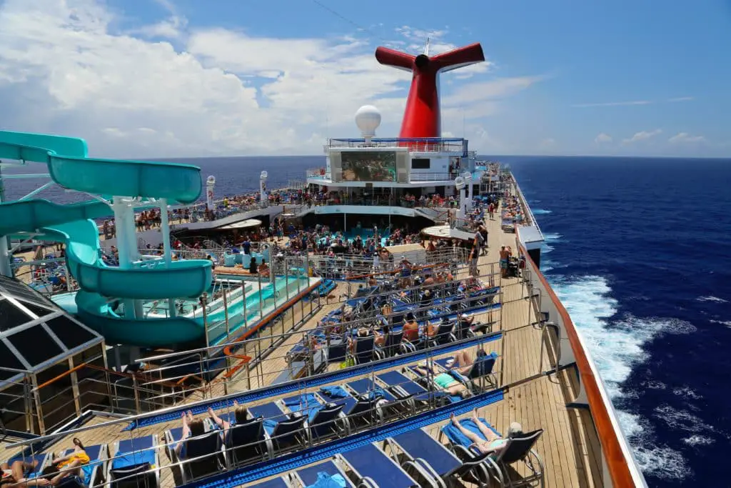 The top deck of a carnival cruise ship . A pool surrounded by deck chairs and a large twisty water slide at one end of the pool