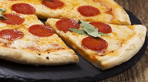 Close-up of a pepperoni pizza, with one slice slightly pulled away from the whole pizza.