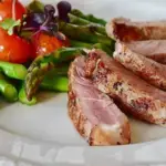 White plate of keto-friendly foods - sliced medium-cooked steak, a pile of asparagus topped with seared cherry tomatoes.