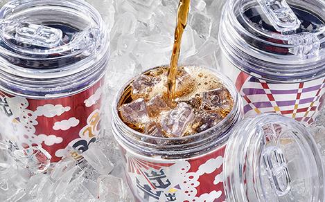 Royal Caribbean souvenir cups filled with soda and ice with a straw stuck out the top. 2 other glasses have their lids on. All are sitting on a bed of ice.